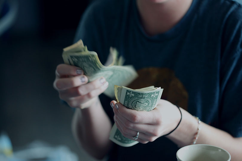 A pair of women's hands holding dollar bills.