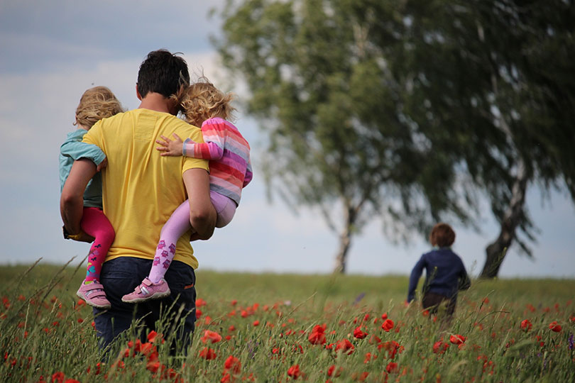 Man carries two small children while following a third in a field of tulips.