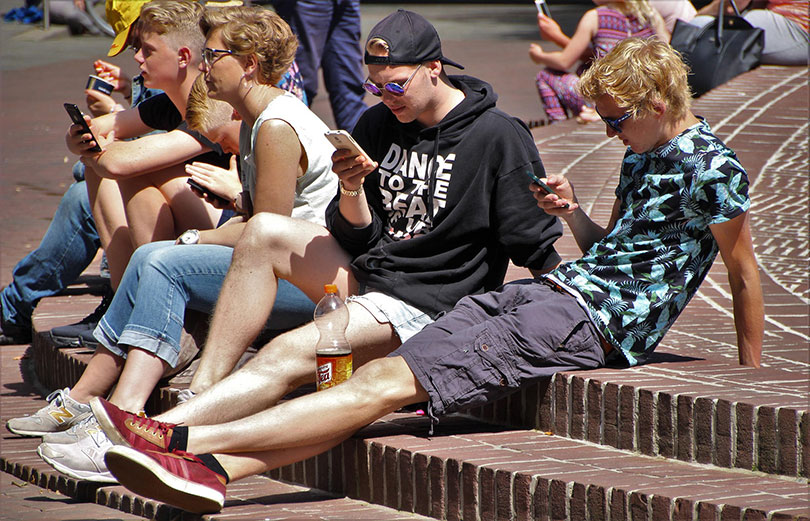 Teens sit on a step at a park looking at their smart phones.