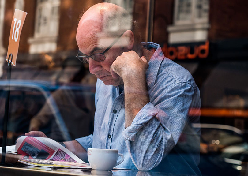 Mature man reads newspaper in a coffee shop.