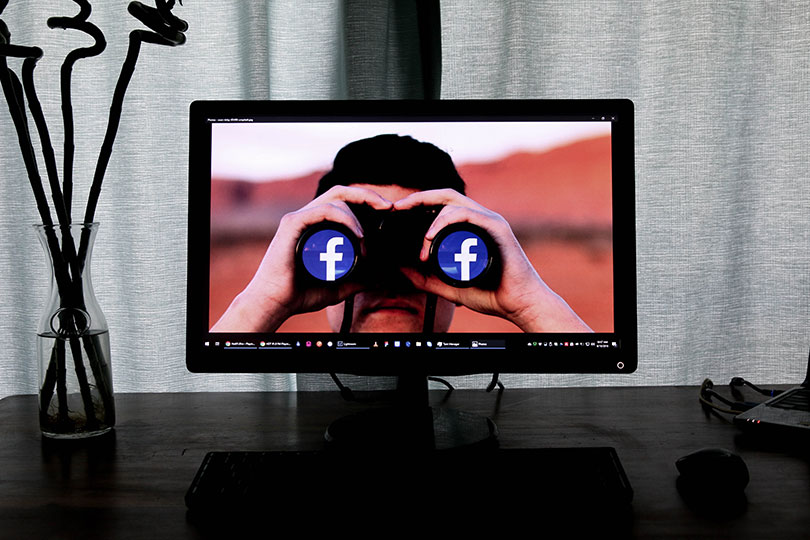 Man holding binoculars that have Facebook’s logo on the lenses.