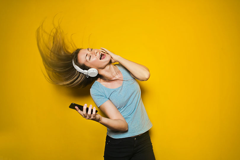 Young woman wearing headphones and holding a mobile phone dancing.