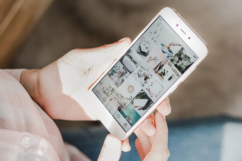 A woman holding a phone looking at an Instagram page.