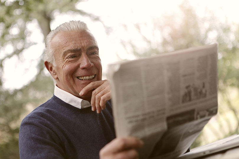 Older man smiling while reading the newspaper. 