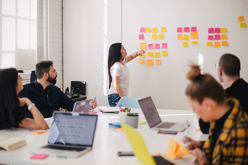 Woman putting sticky notes on whiteboard while in meeting with peers