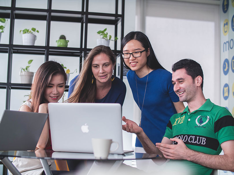 Three women and a man look at computer screen smiling.