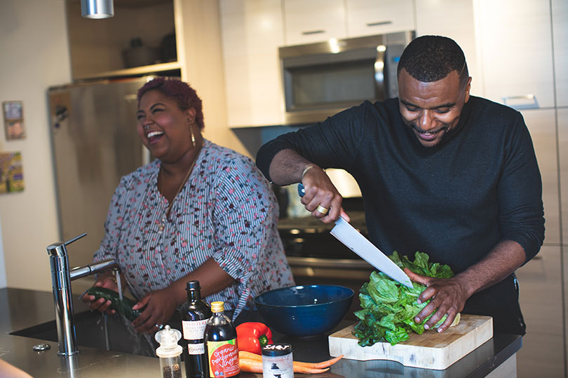 Couple smiles happily while meal prepping in family kitchen.