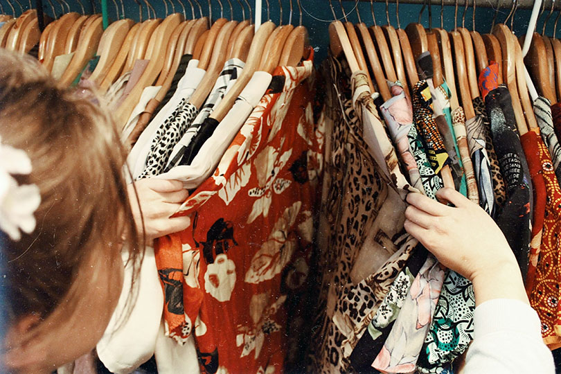 Woman sorting through shirts on a clothes rack in a store. 