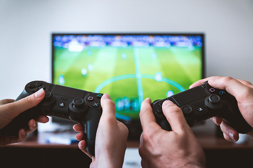 Two sets of hands holding game control devices, facing a TV screen.