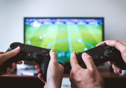 Two sets of hands holding game control devices, facing a TV screen.
