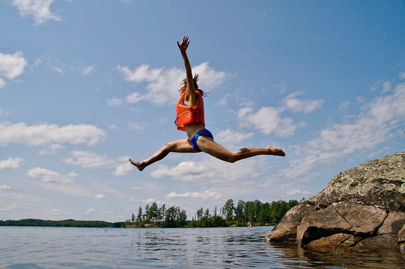 Woman jumping off rocks into water. 