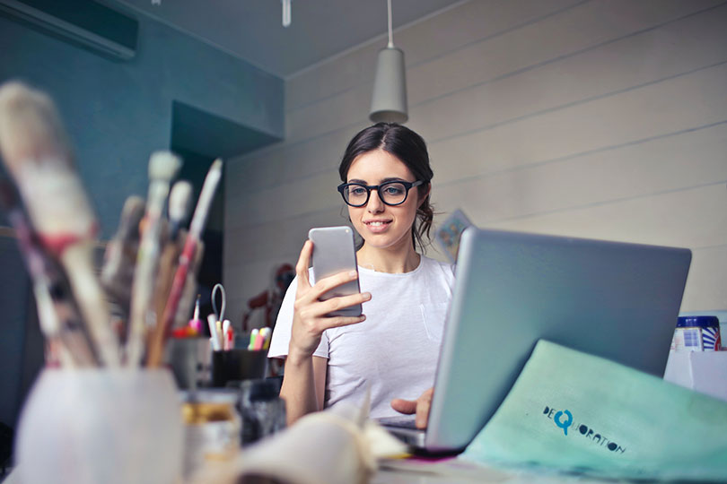 Woman sitting in front of laptop and holding smartphone.