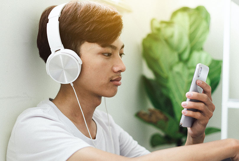 Young man wearing headphones and looking at smartphone screen