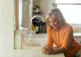 Middle aged woman looking at her smartphone while standing in a kitchen
