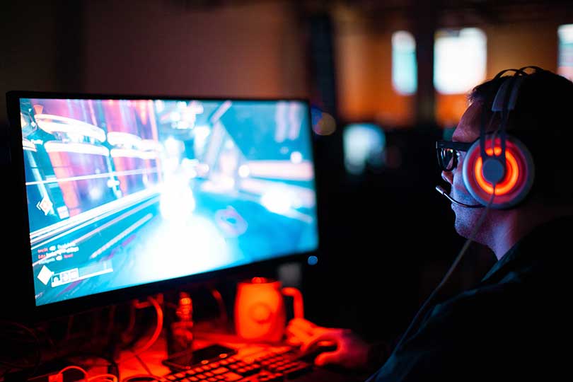 Man wearing headphones, looking at a screen, gaming.