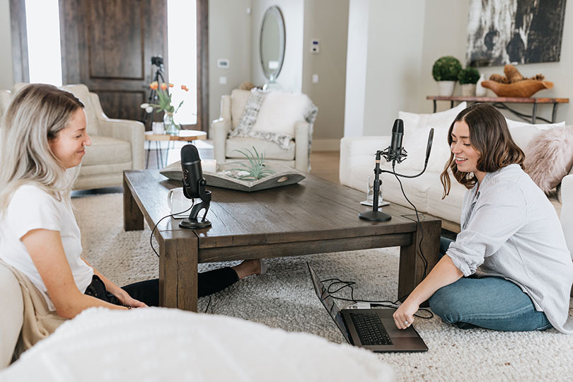 Two women sitting in a living room recording a podcast