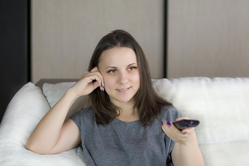 Woman sitting on a couch holding a TV remote