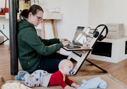 Mom works on a laptop on the floor with a baby by her side.