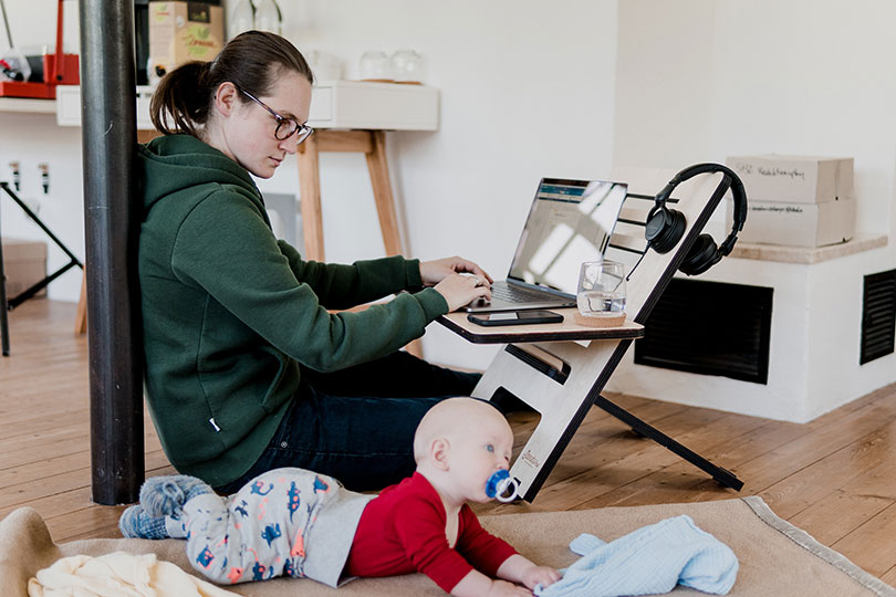 Mom works on a laptop on the floor with a baby by her side.