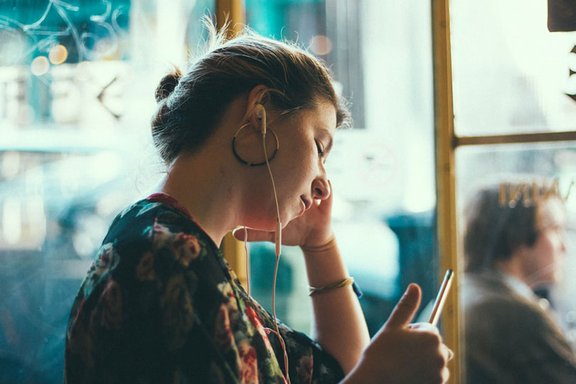 Woman wearing earbuds and holding a mobile phone in a shop