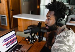 Man wearing headphone and speaking in to a microphone at a laptop