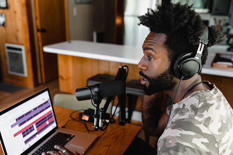 Man wearing headphone and speaking in to a microphone at a laptop